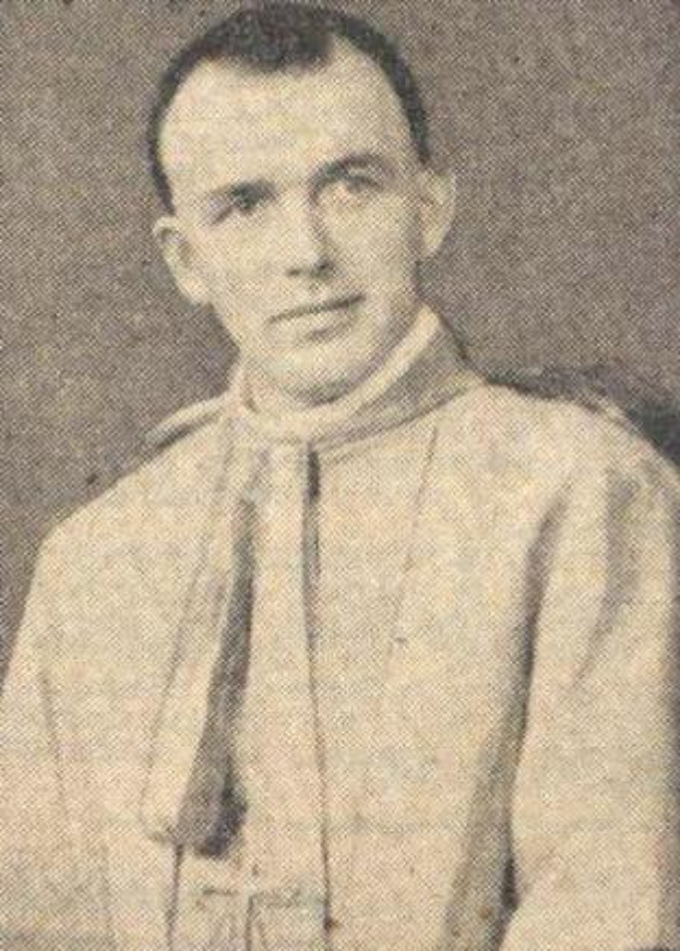 Ein Schwarz-Weiß-Foto eines Mannes in Priesterrobe, der eine weiße Robe mit schwarzem Kragen und Manschetten und einen schwarzen Hut mit einer weißen Feder trägt, mit gefalteten Händen und ernster Miene.