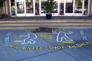 Ein Gebäude mit Glastüren und Fenstern, eine Topfpflanze und ein Schild auf dem Gehweg mit der Aufschrift "Männer erschossen"