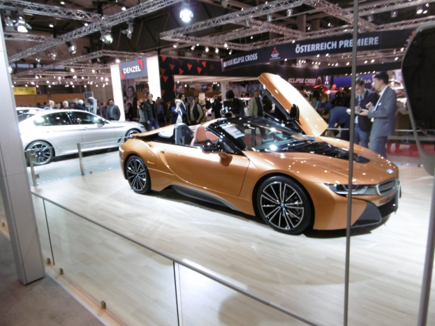 Ein glänzendes, schwarzes BMW i8 Roadster mit Chromakzenten auf der Frankfurter Motor Show umgeben von formell gekleideten Gästen in einer Atmosphäre der Aufregung.