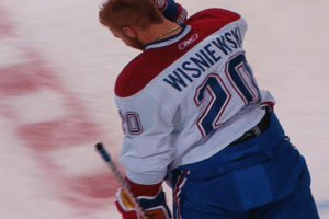 Ein Eishockeyspieler in einem "Wisniewski"-Trikot steht auf dem Eis und hält einen Eishockeyschläger mit konzentrierter Miene.
