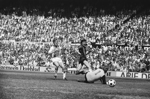 Schwarzes Foto von Männern, die auf einem Feld Fussball spielen, mit Zuschauern im Hintergrund und einem Banner mit der Aufschrift "Bundesliga 1978-79 Ajax 1-1 Hannover 96".