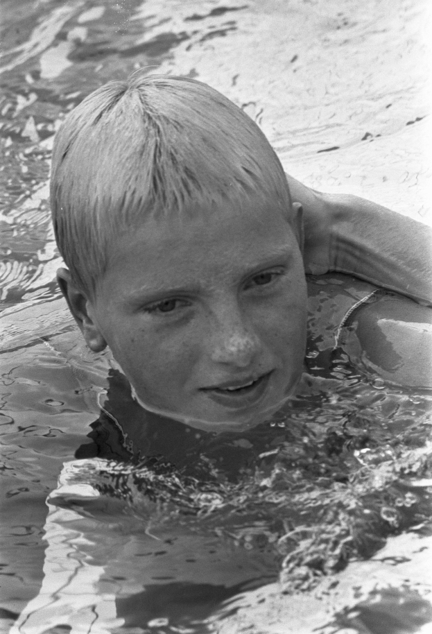 Ein junger Junge schwimmt in einem Pool mit ausgestreckten Armen, sein Gesicht von der Sonne erhellt, während er durch das Wasser gleitet.