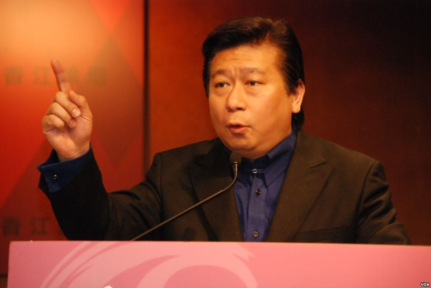 Ein Mann in Anzug und Krawatte, der hinter einem Rednerpult mit Mikrofon spricht und wie einPolitikwissenschaftler mit ernster Miene wirkt.