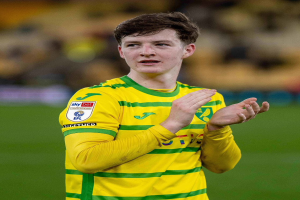 Ein junger Mann in einem gelb-grünen T-Shirt steht auf einem Fußballfeld und klatscht jubelnd in die Hände, mit einem unscharfen Hintergrund.