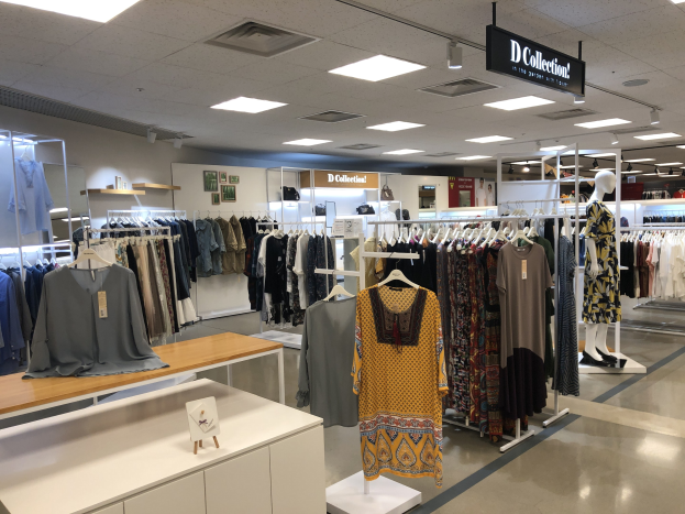 Ein Bekleidungsgeschäft mit Kleidern an Bügeln, Schaufensterpuppen, Tischen mit Auslagen, Wandtafeln und Deckenbeleuchtung, identifiziert als der neue D Collection Store im Mall of America.