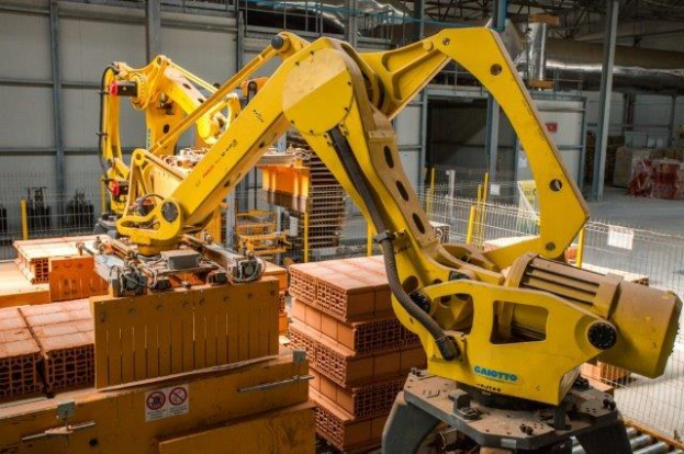 Großes Industrie-Lager mit gestapelten Kisten, Kranen, Zaun, Pfählen und einer fernen Wand in einer automatisierten Fertigungsumgebung.