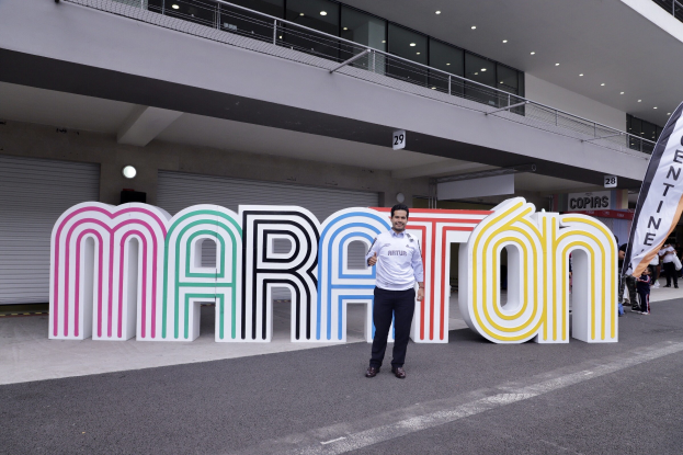 Ein Mann, der vor einem 'Marathon'-Schild strahlt, umgeben von Menschen mit Schildern und einem beleuchteten Gebäude im Hintergrund.