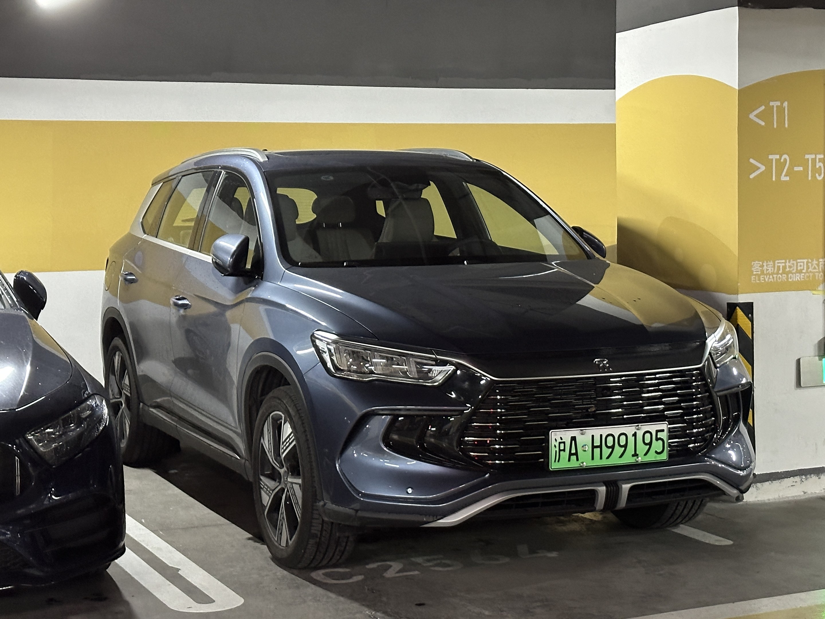 Zwei Autos nebeneinander in einer Garage mit einer Wand und einer Deckenbeleuchtung im Hintergrund, begleitet von einer Texttafel auf der rechten Seite.