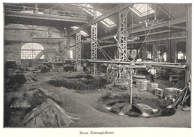 Ein altes Schwarz-Weiß-Foto einer Fabrik mit Arbeitern, die eine Maschine bedienen, umgeben von Metallstangen und -rohren, mit einem Text am unteren Rand, der "Neue Eisenglebeerei, die erste Fabrik in Deutschland" lautet.