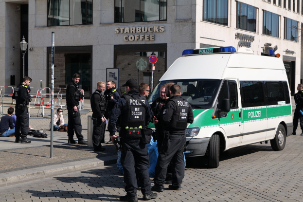 Polizisten vor einem Starbucks-Café mit einem Van auf der rechten Seite und Menschen auf der linken Seite, mit einem Gebäude, einem Schild, einem Laternenmast und einem Zaun im Hintergrund.