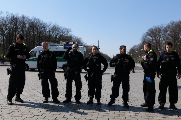 Eine Gruppe von Polizeibeamten steht vor einem Rettungswagen auf einer von Bäumen gesäumten Straße unter einem klaren Himmel.