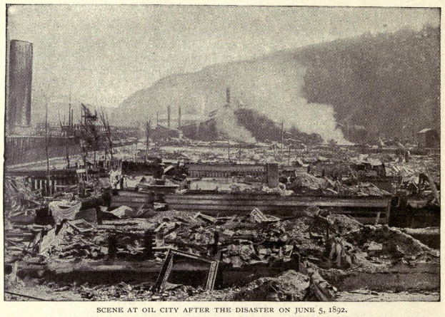 Schwarz-weiß-Foto einer Stadt nach einer Katastrophe am 5. Juni 1892, das beschädigte Gebäude, Strommasten, Rauch und einen Hügel im Hintergrund zeigt, mit Text am unteren Rand.