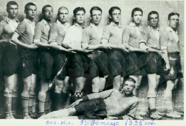 Ein Schwarz-Weiß-Foto einer Fußballmannschaft mit einem Mann in der Mitte auf dem Boden liegend und Text unten.