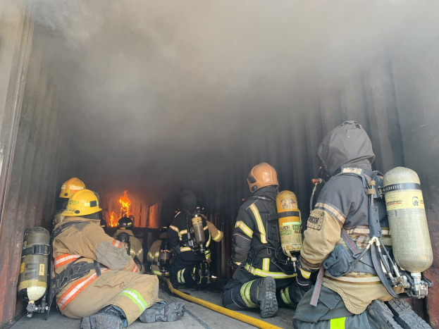 Feuerwehrleute in Helmen und Sauerstoffflaschen sitzen im Heck eines raucherfüllten Trucks während einer Übung an der University of California, Berkeley, mit einem großen Feuer im Hintergrund.