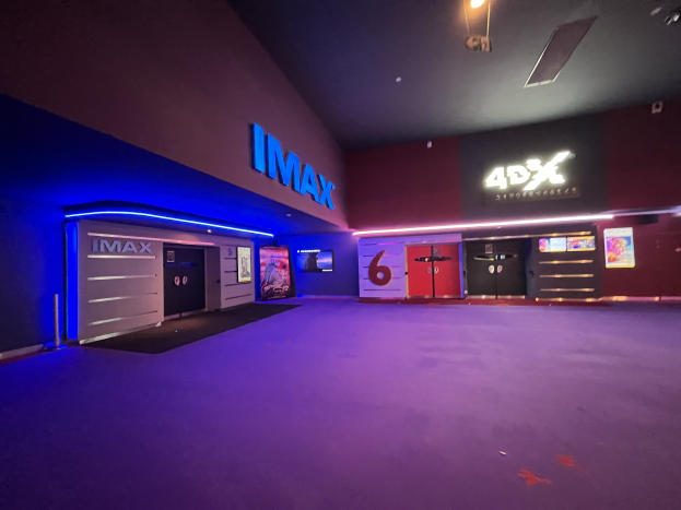 Innenseite eines Kinos mit lila Teppich, Text und Bildschirmen an den Wänden und Deckenleuchten.