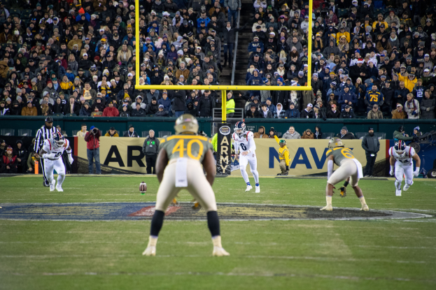Fußballspieler mit Helmen und Uniformen auf dem Feld mit Zuschauern in den Rängen und Stadionwerbung im Hintergrund.