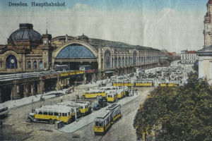 Eine alte Postkarte zeigt einen belebten Dresdner Bahnhof mit Fahrzeugen, Menschen, Bäumen, Gebäuden und einer bewölkten Himmel, mit der Aufschrift "Dresden Hauptbahnhof" oben.