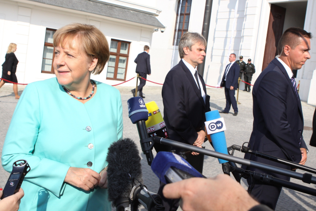 Bundeskanzlerin Angela Merkel spricht mit Reportern ├Ąußerhalb des Kanzleramts in Berlin, umgeben von Menschen mit Mikrofonen und Geb├Ąuden im Hintergrund.