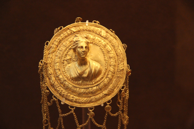 Goldene Medaille mit einer Frauengestalt auf dunklem Hintergrund, mit aufwendiger und luxuriöser Verzierung.