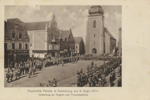 Ein Schwarz-Weiß-Foto eines Umzugs in Insterburg am 5. September 1914 mit vielen Menschen, Gebäuden im Hintergrund und Text unten.