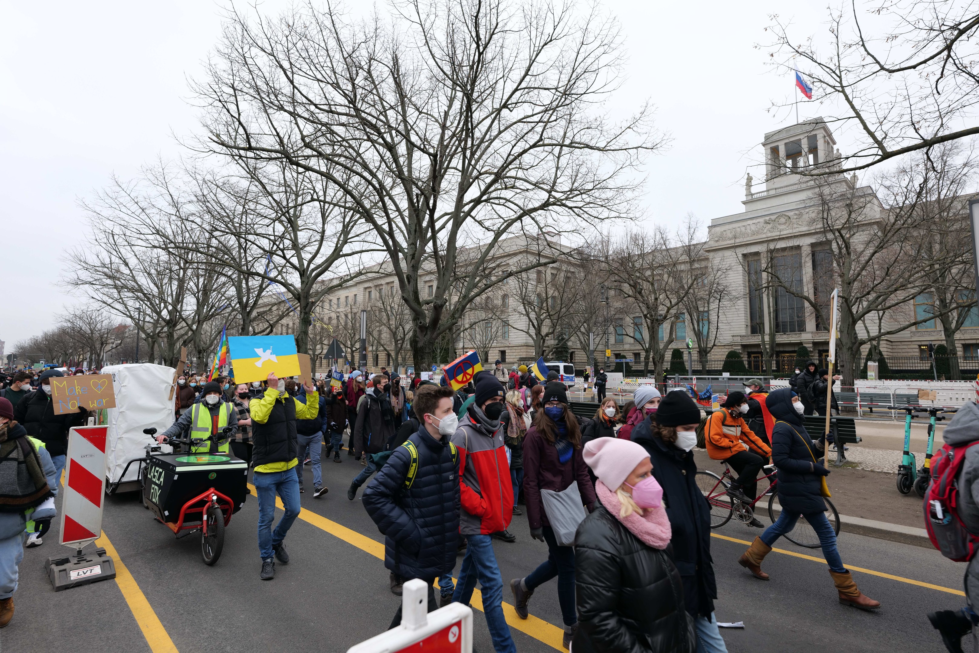 Eine große Gruppe von Menschen marschiert bei einer Protestaktion auf einer Straße in Washington, D.C., mit Schildern und Transparenten, einige fahren Fahrräder, unter einem klaren blauen Himmel.