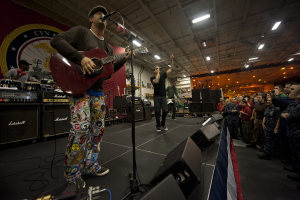 Ein Mann, der als Chris Stapleton identifiziert wird, spielt eine E-Gitarre auf der Bühne vor einem Publikum, trägt eine Mütze und ist von einem Mikrofon, Lautsprechern, einer Flagge und anderen Instrumenten umgeben.