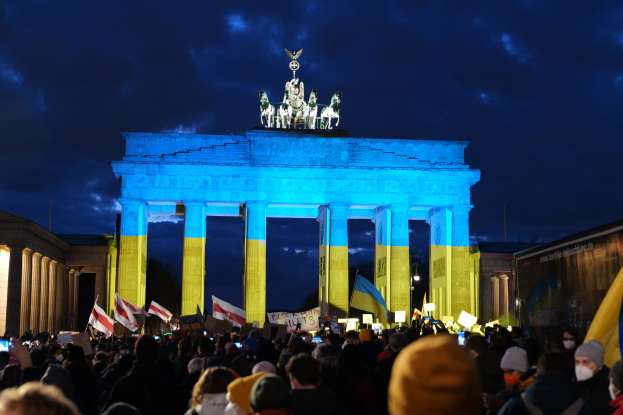 Eine Menschenmenge steht vor dem Brandenburger Tor in Berlin, Deutschland, mit Fahnen und Schildern, mit einer Banner auf der rechten Seite des Bildes.