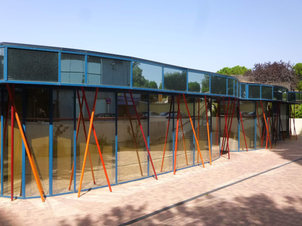 Ein modernes Schulgebäude mit zahlreichen Fenstern, einem vorderen Weg, der mit Bäumen gesäumt ist, und einem klaren blauen Himmel darüber.