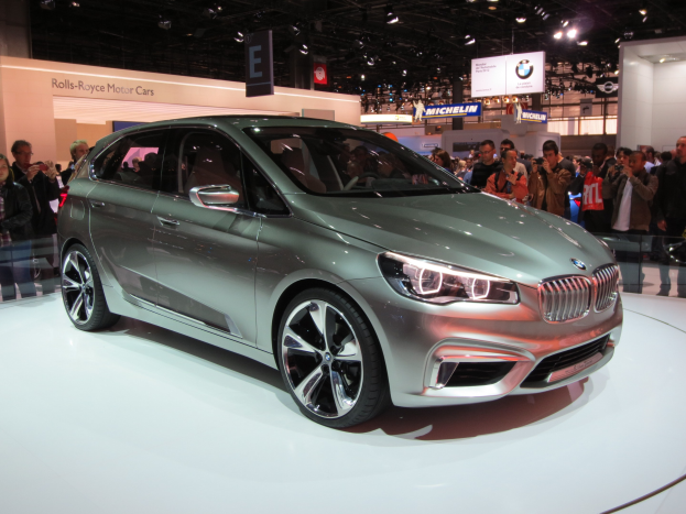 Ein BMW 2er Active Tourer Concept auf der IAA in Frankfurt, umgeben von Menschen, die Fotos machen, unter Deckenleuchten mit Texttafeln im Hintergrund.