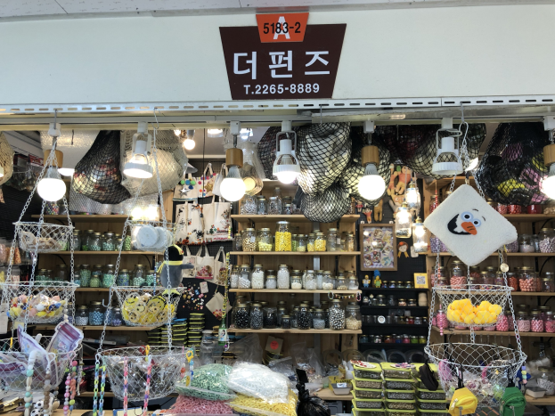 Ein unordentlicher Laden in Seoul mit verschiedenen Gegenst%C3%A4nden wie K%C3%B6rbchen, Lichtern, Flaschen und Spielzeugen auf Regalen, mit einer Tafel oben, die ihn als einen der besten koreanischen L%C3%A4den kennzeichnet.