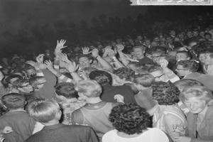 Ein Schwarz-Weiß-Bild einer Menge auf einem Konzert mit erhobenen Händen um eine Tafel mit Text.