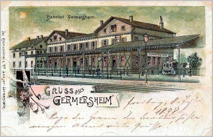 Schwarz-weiß-Postkarte des Bahnhofs Germersheim in Deutschland, die ein Gebäude mit Fenstern, einen Zaun, einen Straßenpfahl, eine Gruppe von Menschen, Fahrzeuge auf der Straße, Bäume und einen bewölkten Himmel zeigt.