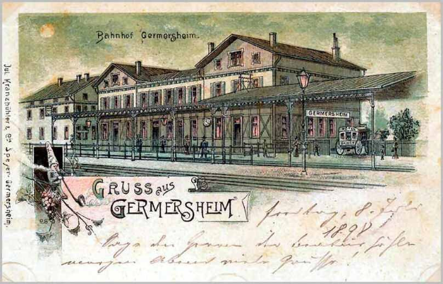 Schwarz-weiß-Postkarte des Bahnhofs Germersheim in Deutschland, die ein Gebäude mit Fenstern, einen Zaun, einen Straßenpfahl, eine Gruppe von Menschen, Fahrzeuge auf der Straße, Bäume und einen bewölkten Himmel zeigt.