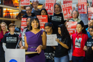 Eine Black-Lives-Matter-Aktivistin spricht in ein Mikrofon an einem Podium mit einer Tafel, vor einer Menge mit Schildern.