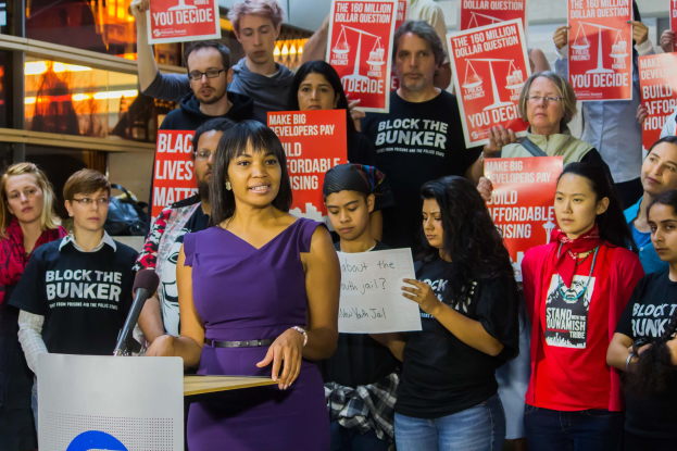 Eine Black-Lives-Matter-Aktivistin spricht in ein Mikrofon an einem Podium mit einer Tafel, vor einer Menge mit Schildern.
