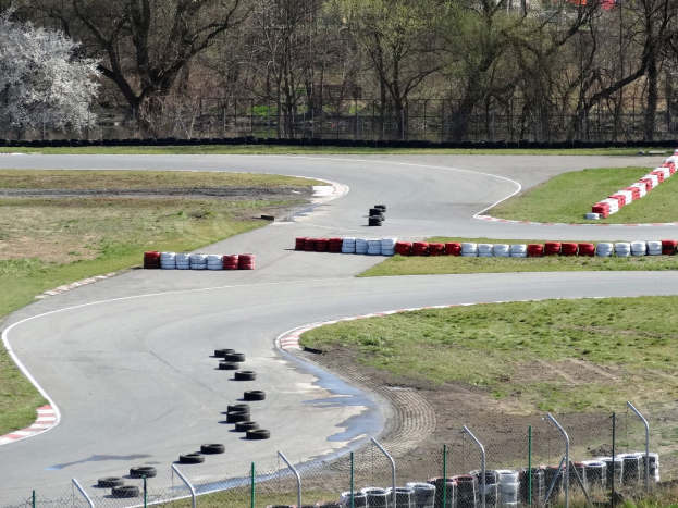 Rennstrecke voller Reifen, gesäumt von Gras und Maschendrahtzaun, mit Bäumen im Hintergrund.