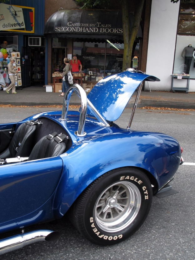 Ein blaues Fahrzeug, das auf einer Straße mit Geschäften und Menschen im Hintergrund fährt.