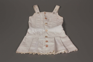 Weißes Kleid mit runder Halsausschnitt, kurzen Ärmeln und vollem Rock mit symmetrischen Knöpfen und dezentem Glanz auf grauer Oberfläche.