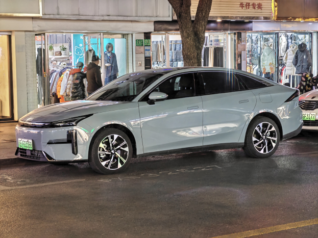 Elektrischer Mitsubishi Lancer EV auf einer nächtlichen Stadtstraße mit umliegenden Gebäuden, Schaufenstern, Schaufensterpuppen und beleuchteten Schildern.