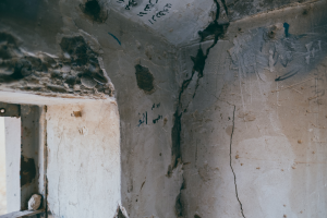 Ein Raum mit einem Fenster auf der linken Seite und einer Wand mit einem durchlaufenden Riss, bedeckt mit Graffiti.