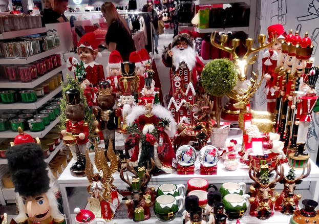 Ladeninneres mit Weihnachtsdekorationen, einschließlich Spielzeug, Tassen und anderen Gegenständen auf Tischen und Regalen, mit Menschen, Lichtern und einer Wand im Hintergrund.