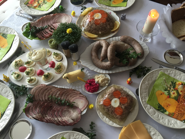 Ein langer Tisch mit verschiedenen Gerichten, Besteck, Gläsern und Kerzen, umgeben von Stühlen, das einen traditionellen deutschen Osterbrunch vermuten lässt.