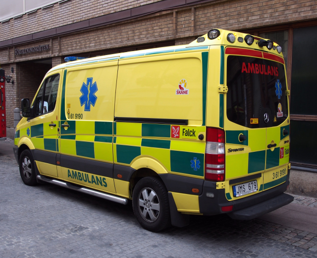 Ambulanz auf der Straße vor einem Backsteingebäude mit Text, mit einem Feuerlöscher auf der linken Seite.