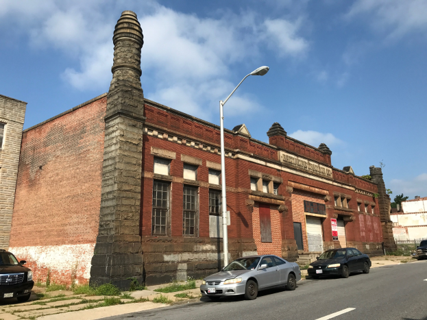 Außenansicht einer ehemaligen Feuerwache in St. Louis, ein altes Backsteingebäude mit seitlichem Schornstein, umgeben von Straßenlaternen, Fahrzeugen, Infotafeln, Bäumen und einem bewölkten Himmel.