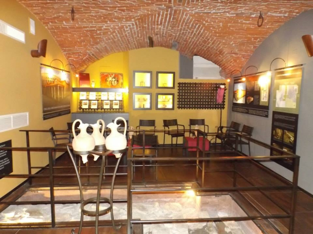 Ein geräumiger Museumsraum mit zahlreichen Tischen, Stühlen, Displaytafeln, gerahmten Kunstwerken, Vasen und Deckenbeleuchtung.