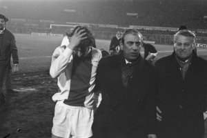 Eine Gruppe verzweifelter Männer in Schwarz-Weiß-Kleidung steht zusammen auf einem Fußballfeld, im Hintergrund ein Stadion, wahrscheinlich nach einem gewonnenen Spiel.
