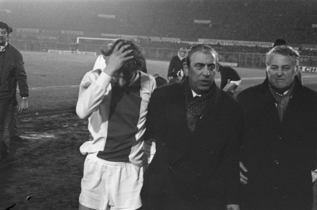 Eine Gruppe verzweifelter Männer in Schwarz-Weiß-Kleidung steht zusammen auf einem Fußballfeld, im Hintergrund ein Stadion, wahrscheinlich nach einem gewonnenen Spiel.
