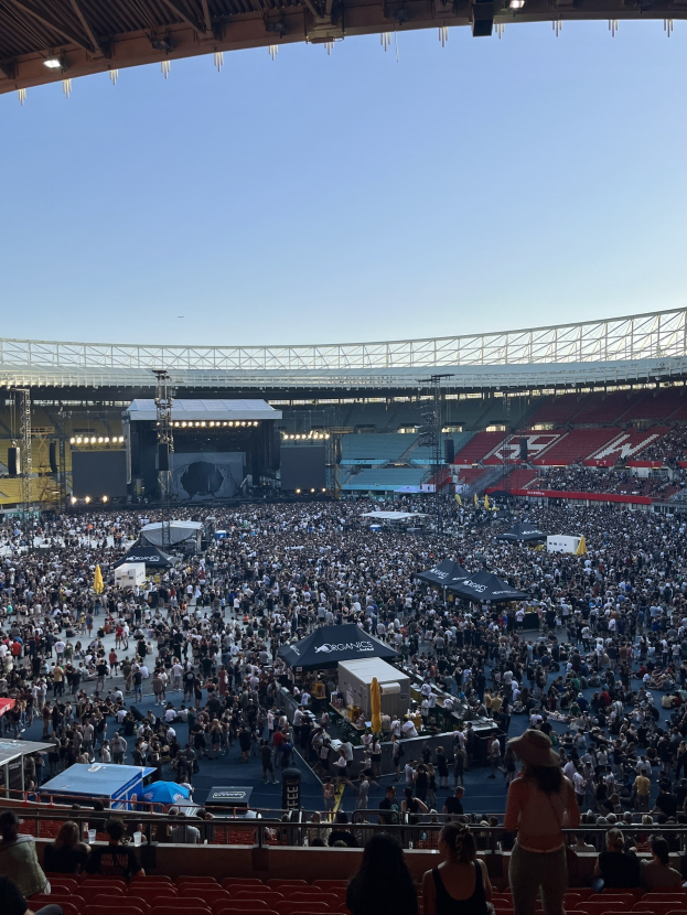 Große Menge sitzend und stehend in einer Halle mit Geländern, Zelten und Deckenbeleuchtung, vor einem sichtbaren Himmel im O2 Arena in London.