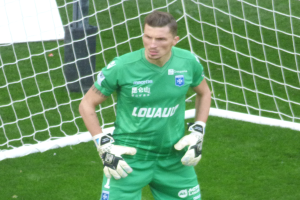 Ein Torwart in grüner Uniform steht vor einem Fußballtor auf saftigem Grün, Handschuhe tragend.