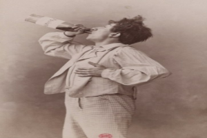 Ein altes Schwarz-Weiß-Foto eines Mannes mit ernstem Gesichtsausdruck, der aus einer Flasche trinkt.